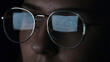 Woman use laptop computer and reading an article at night. Concept. Close up of young female face with big glasses and the reflection of the monitor in lenses isolated on black background.