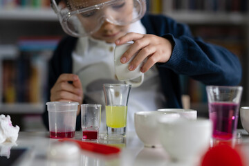 Close up on hand of One small caucasian boy scientist five years old sitting at the table playing with chemistry equipment toy preforming experiment learning and education concept front view