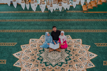 Muslim father with two child daughters reading a holy book Quran inside the Mosque. 