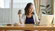© bongkarn - Attractive asian senior aged woman using portable laptop, drinking her morning coffee.