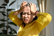 © bongkarn - Unwell middle-aged Asian female touch her head, suffer from migraine headache.