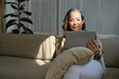 © bongkarn - Relaxed asian aged-woman resting in her living room, sitting on comfy sofa and using tablet