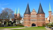 canvas print picture - Lübeck Holstentor mit Spitztürmen und Kirchtürmen in Grünanlage unter blauem Himmel