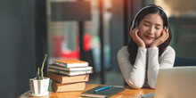 Female Asian College Student Wearing Headphones Enjoys Online Music.
