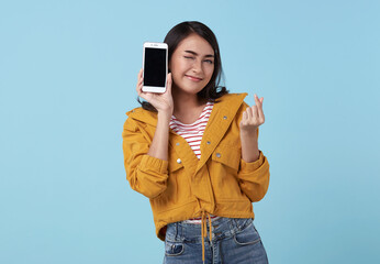 Happy young Asian woman showing at blank screen mobile phone and mini heart isolated over blue background.