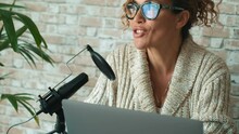 Modern lady speaking at the microphone recording podcast at home using laptop computer. Online new job business freelance for smart working and office freedom concept lifestyle. People and technology