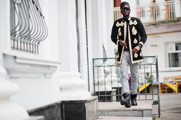 Wall Mural - Mega stylish african man in traditional jacket pose. Fashionable black guy in hat and sunglasses with cigar in hand.