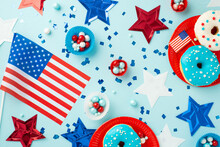USA Independence Day Concept. Top View Photo Of National Flags Star Garland Confetti Paper Backing Molds With Candies And Plate With Glazed Donuts On Isolated Pastel Blue Background