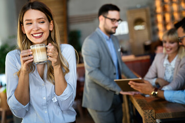 Wall Mural - Portrait of happy young business woman drinking coffee in a break. In the background, her colleagues