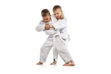 Dynamic Portrait Of Two Little Boys, Taekwondo Or Karate Athletes Wearing Doboks Training Together Isolated On White Background. Concept Of Sport, Martial Arts