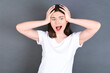 © Jihan - Horrible, stress, shock. Portrait emotional crazy young beautiful Caucasian woman wearing white T-shirt over studio grey wall clasping head in hands. Emotions, facial expression concept.