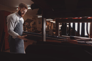 Wall Mural - Man shoemaker hold different rolls natural leather brown, working with textile in workshop