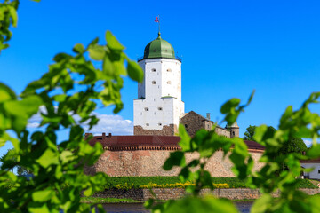Poster - Medieval fortress in Vyborg. Castle on the water against the blue sky with green foliage