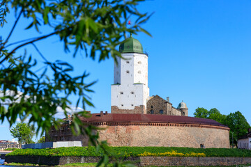Poster - Medieval fortress in Vyborg. Castle on the water against the blue sky with green foliage