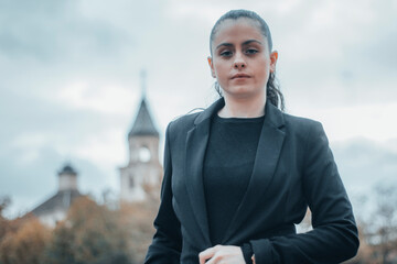 Mujer empresaria joven de cabello moreno formal con seriedad y de pie con posición femenina pensando seria en el centro de la ciudad parada por la calle para llegar a su trabajo