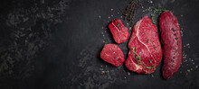 Assortment Of Raw Cuts Of Raw Beef Meat Steaks With Spices On A Dark Background. Long Banner Format. Top View