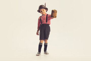 Wall Mural - Portrait of stylish little boy, child in checkered shirt and shorts holding wooden mug isolated over grey studio background