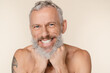 © InsideCreativeHouse - Closeup cropped image of smiling with toothy smile caucasian middle-aged mature man shirtless with tattoo and grey hair beard isolated in beige background. Male body beauty care