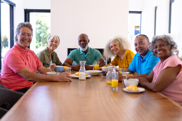 Wall Mural - Portrait of happy multiracial senior friends with food and drink on dining table in nursing home