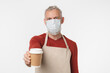 © InsideCreativeHouse - Coronavirus takeout take away food concept. Caucasian mature middle-aged man in apron barista selling giving coffee hot beverage tea in paper cup in protective mask isolated in white background