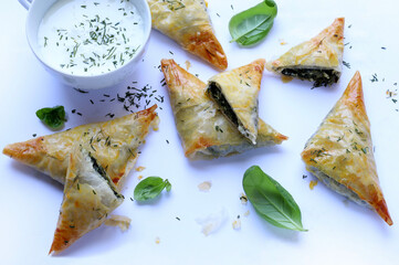 Cucina tradizionale greca. Spanakopita, triangoli croccanti di pasta fillo con spinaci, feta, aneto e salsa tzatziki su sfondo bianco Direttamente sopra.