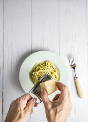 Spaghetti italiani with fresh homemade pesto sauce. Two hands grating a grana cheese. All on a white wooden table.