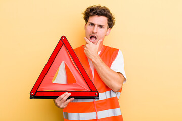 Wall Mural - young handsome guy with mouth and eyes wide open and hand on chin. car emergency triangle concept