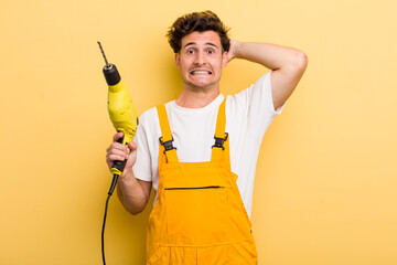 young handsome guy feeling stressed, anxious or scared, with hands on head. handyman with a drill concept