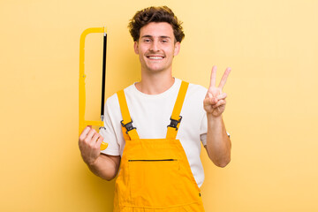 young handsome guy smiling and looking friendly, showing number two. handyman and a saw concept