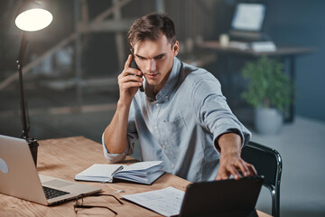 Wall Mural - young businessman talking on a smartphone and using a laptop .