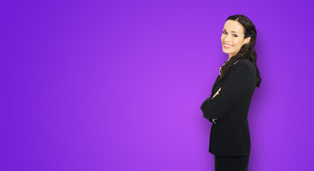 Wall Mural - Happy smiling attractive businesswoman, with copy space area for some slogan or advertising text. Confident brunette woman in black suit standing on violet purple background. Business ad concept.