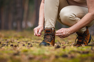 Wall Mural - woman tying shoelace on her hiking boot. tourist is getting ready for hike at forest trekking trail