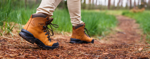 Wall Mural - Tourist with hiking boots walking on footpath in forest. Trekking trail in woodland. Waterproof leather ankle boot. Panoramic view