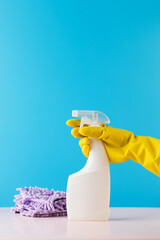 A hand in a yellow glove holds a spray bottle mockup with detergent on a blue. Cleaning, cleaning service. Copy space.