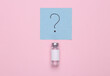 © splitov27 - Medicine concept. Vaccine bottle with a question mark on a memo paper on a pink background. Top view