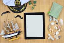 Marine Theme ,vacation Near The Sea Concept. Digital Tablet Mockup With White Blank Screen, Wooden Model Ship, Textile Bag With Sea Shells , White 
Captain Hat  On Bamboo Straw Background .Top View.