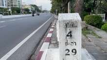 Traffic Concrete Distance Road Sign On Road Side Ground With Vehicles On Road Daytime. Display 4 Kilometer To Hua Hin And 29 Kilometer To Cha Am
