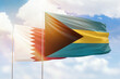 Sunny blue sky and flags of bahamas and qatar