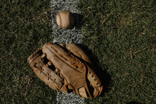 Old Baseball Glove With Ball On Foul Line Of Outfield Grass With Copy Space On Sports Background.