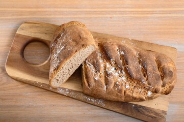 Fresh bread just cooked at home in the kitchen, cut into two large pieces, lies on a wooden board. 