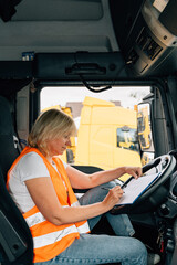 Wall Mural - Mature woman truck driver steering wheel inside lorry cabin. Happy middle age female trucker portrait 