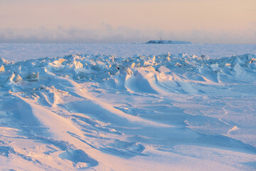 Wall Mural - Winter arctic landscape. Cold frosty winter weather. Harsh polar climate. Ice hummocks on the frozen sea in the Arctic. View of snow and ice at sunset. A small island in the distance. Far North.