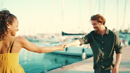 Wall Mural - Close-up of young happy man and woman joyful dancing on the embankment on yacht background. Closeup, joyful date of a young interracial couple. Camera moves around people