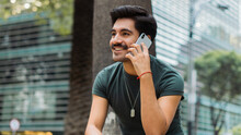Latin Man With Mustache Smiling, Sitting On A Bench Making A Phone Call.