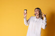 © kamonrat - Cheerful Asia woman with curly hair wear white sweater feel wow about something and holding paper cup of hot coffee or tea takeaway. Studio pastel yellow background.