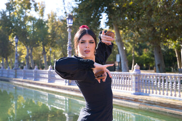 Woman dancing flamenco with black gypsy costume with yellow polka dots and red flower in her hair and castanets in her hands in seville. Concept of flamenco cultural heritage of humanity.