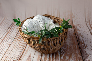 brown wicker basket for a newborn photo shoot on a wooden background. props for a photo shoot, decorated with olive branches. knitted rug