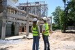 Rear view civil engineer team wearing yellow vests is discussing the construction process together at construction site