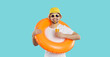 Happy young man with inflatable swimming circle and with glass of juice enjoys summer vacation. Cheerful funny guy in summer clothes drinks juice on light blue background. Summer relaxation concept.