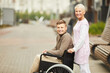 © Mediaphotos - Positive mature blond nurse in uniform pushing wheelchair with smiling young patient in medical hospital yard